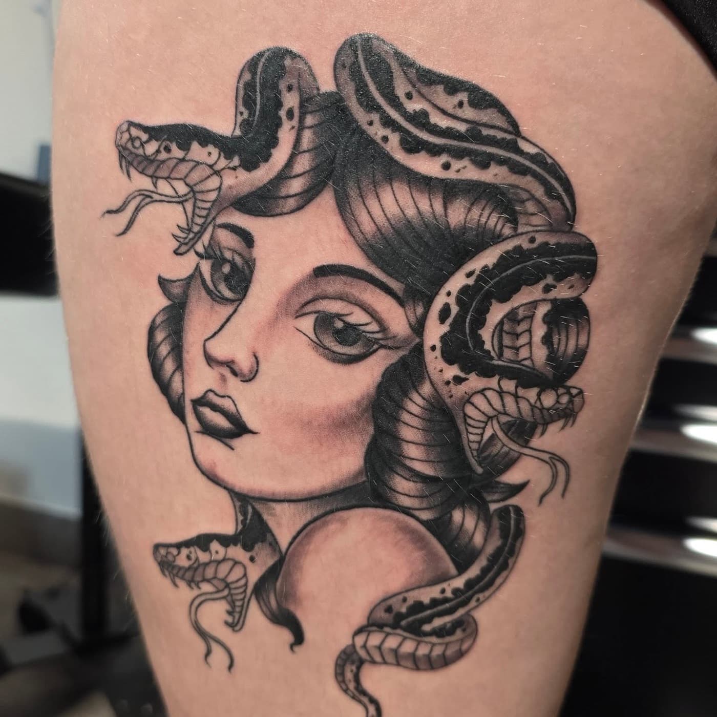 Medusa with snakes coiling through her hair, black and grey on a thigh