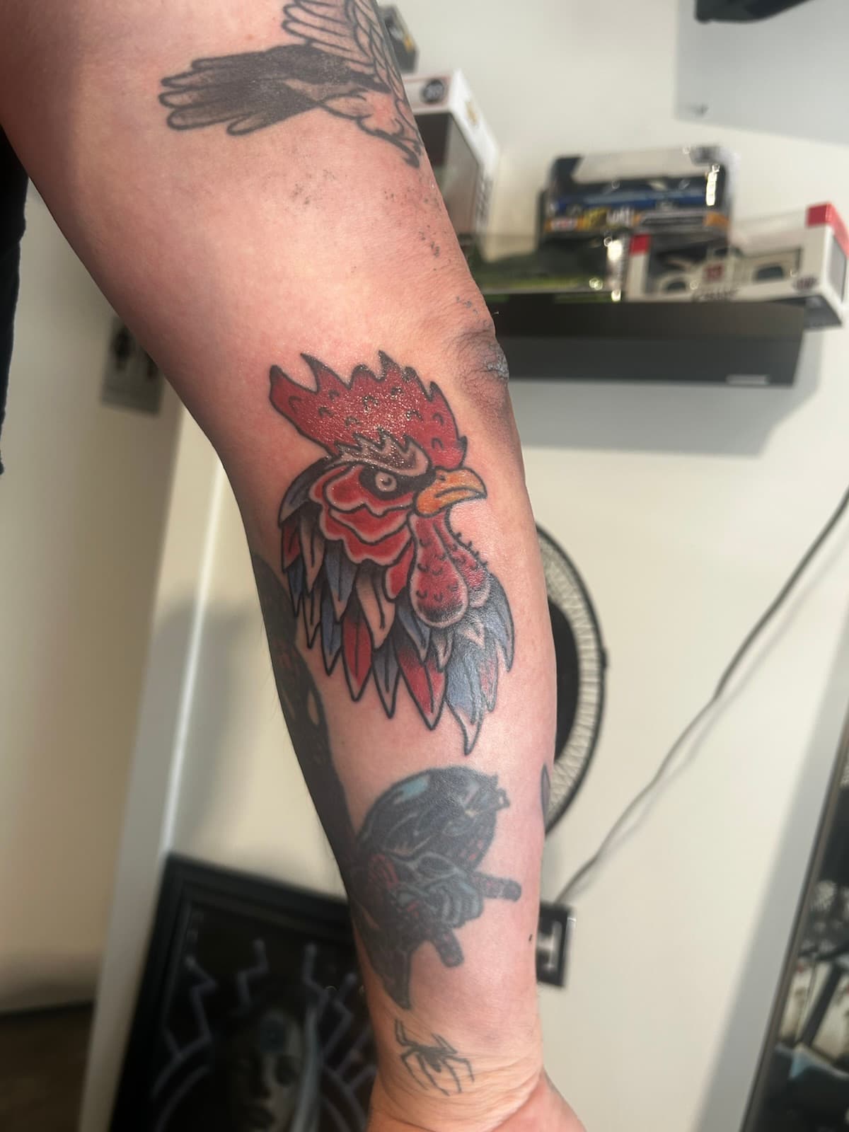 Rooster head with red comb and blue-tipped feathers, colour on the forearm