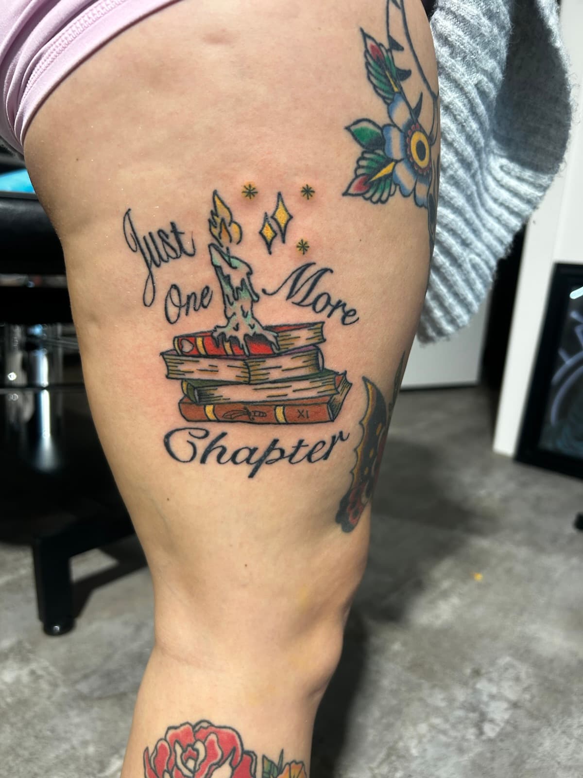 Stack of books under a dripping candle, 'Just One More Chapter' in script, on the thigh
