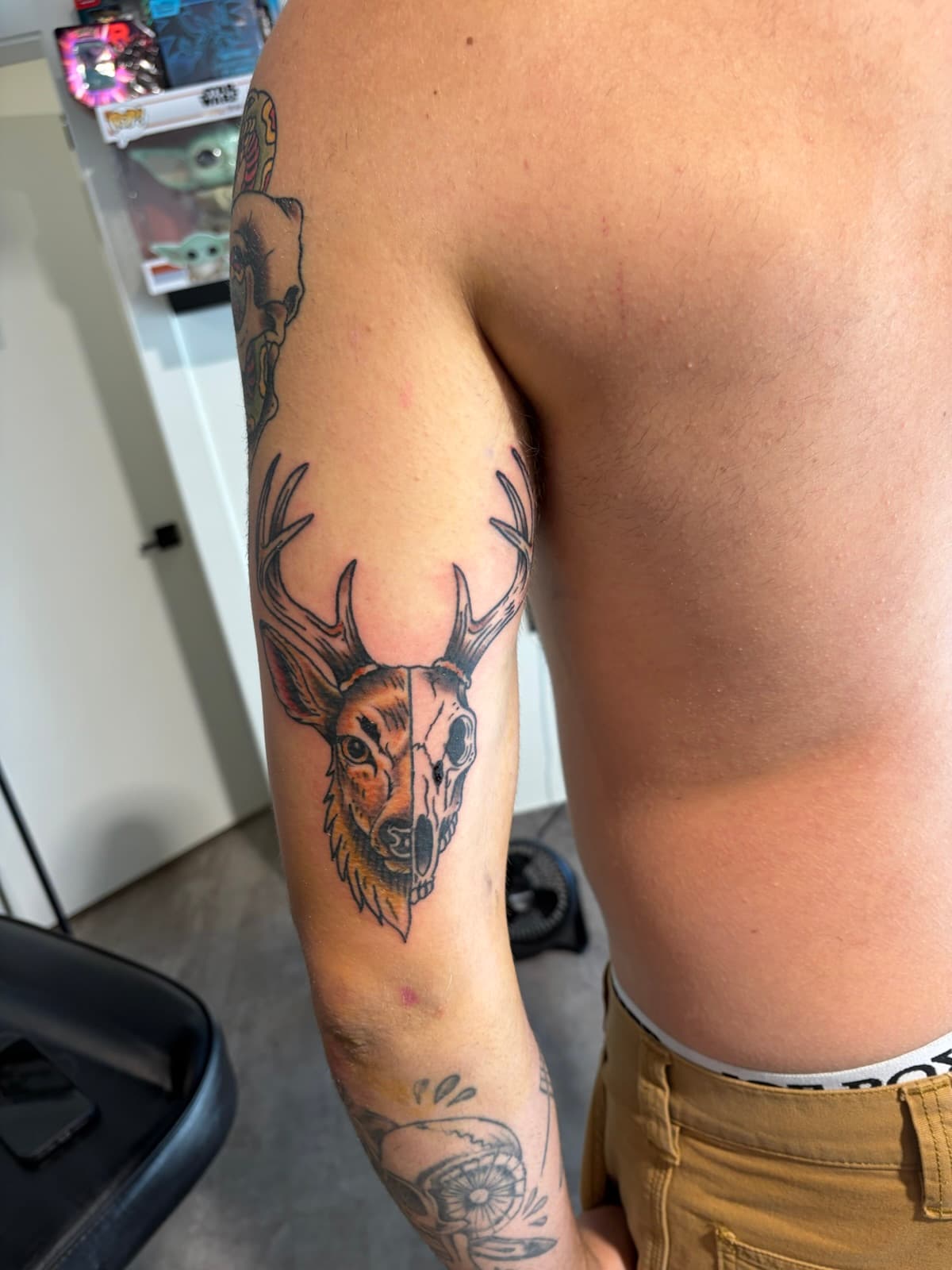Stag head split down the middle, half fur and half skull, on the back of the upper arm