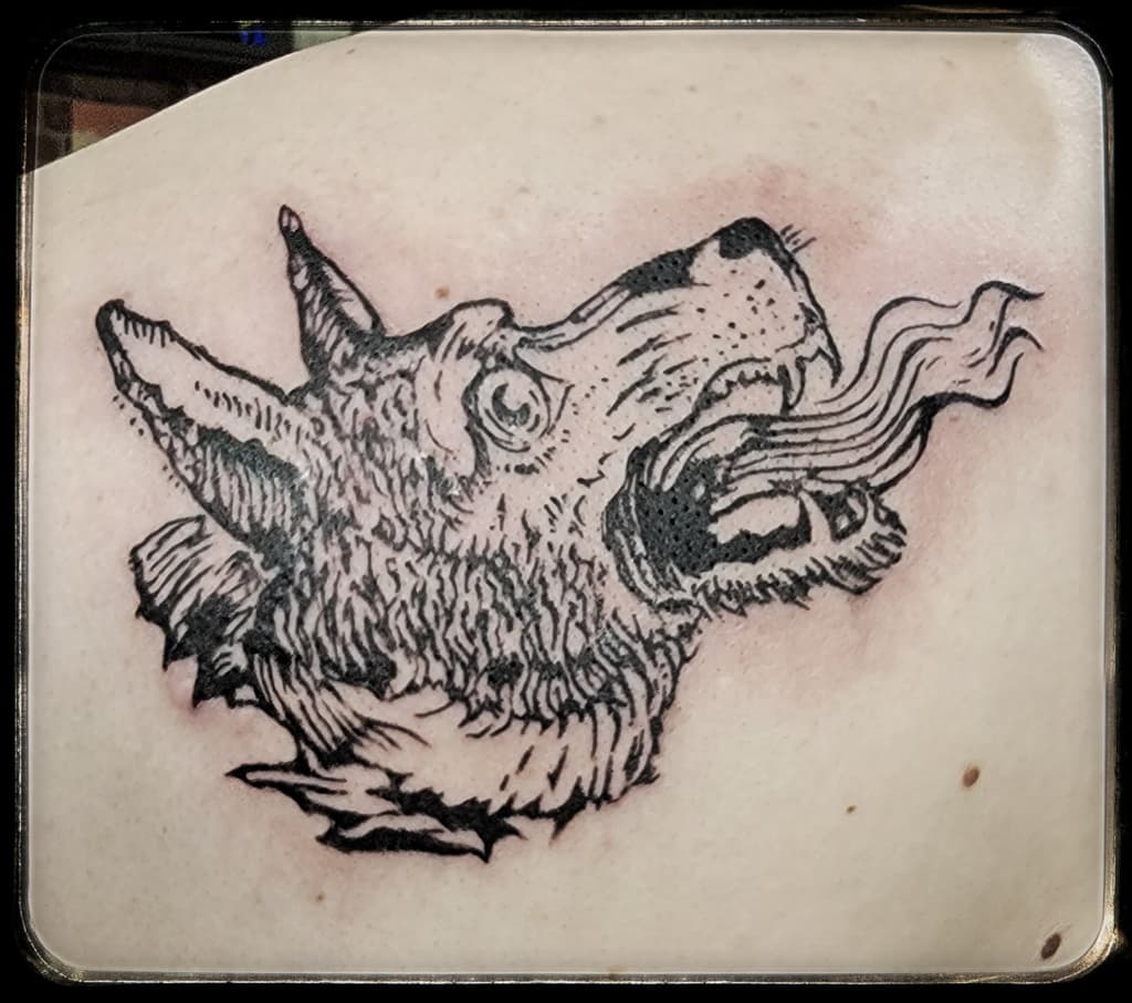 Canine head with long ears and open jaws breathing smoke, black etched linework on the upper chest