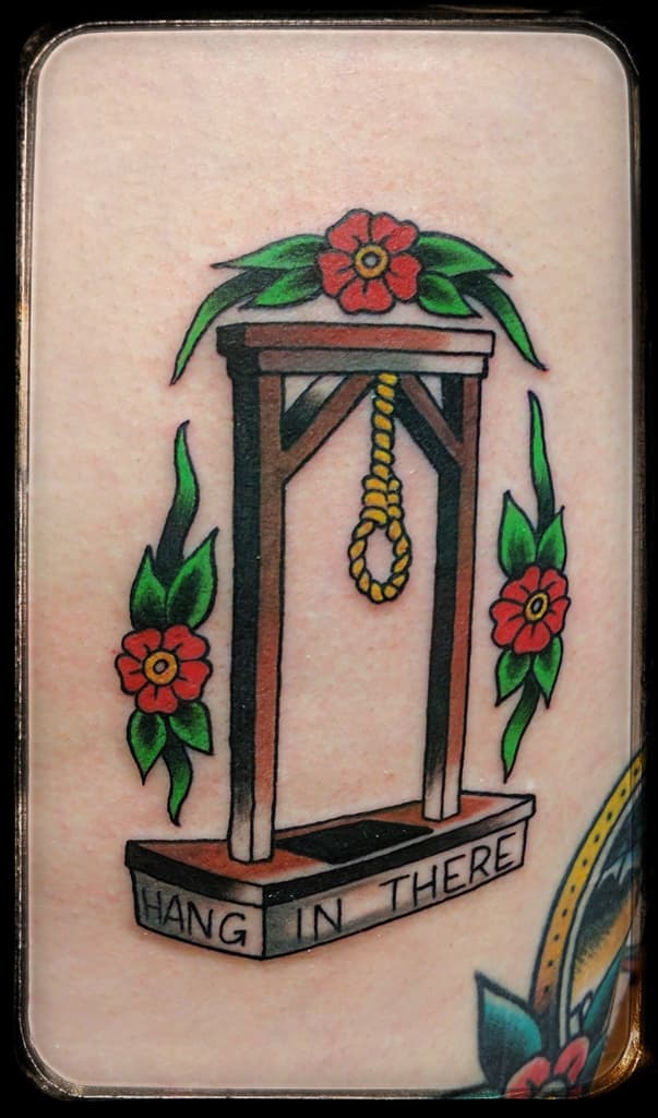 Gallows with a noose framed by red flowers, ‘Hang in there’ on the base, traditional colour