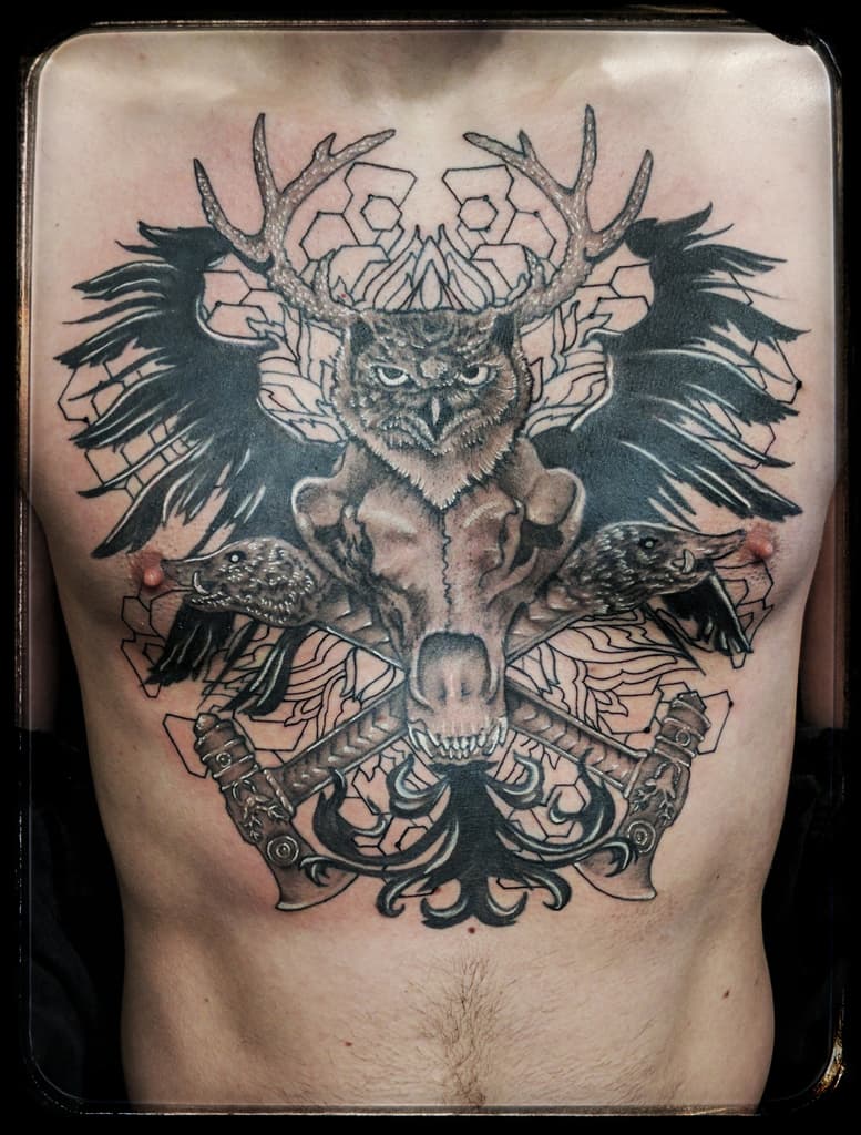 Chest piece of an antlered owl over an animal skull, boar heads, crossed axes and black wings, black and grey