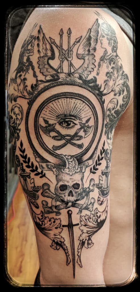 Eye over crossed axes inside a ring, with skull and crossbones, dagger, ships and laurels, black and grey etching on the upper arm