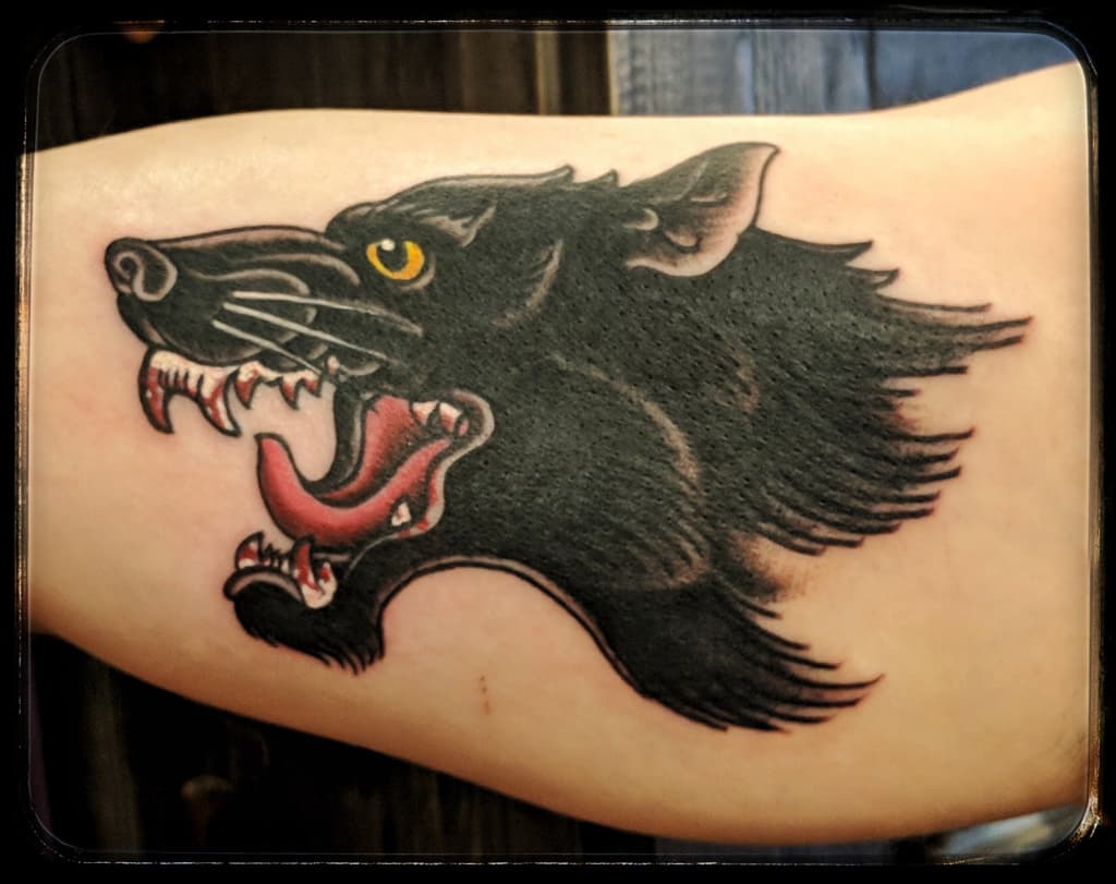 Black wolf head snarling with yellow eye and red tongue, traditional colour on the arm
