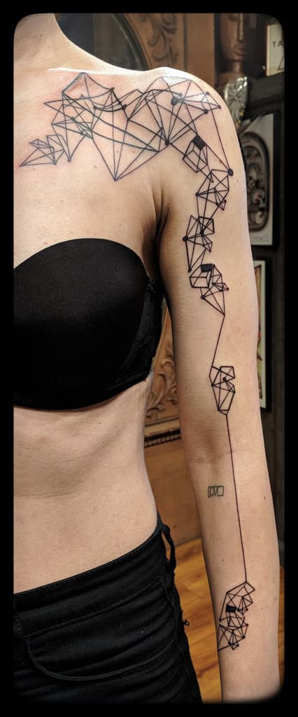 Geometric polyhedra joined by thin lines across the collarbone and down the arm to the wrist, black linework