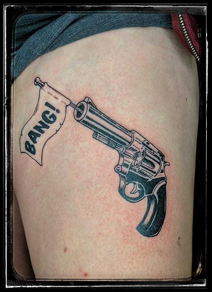 Revolver with a BANG! flag coming out of the barrel, black and grey on the upper thigh