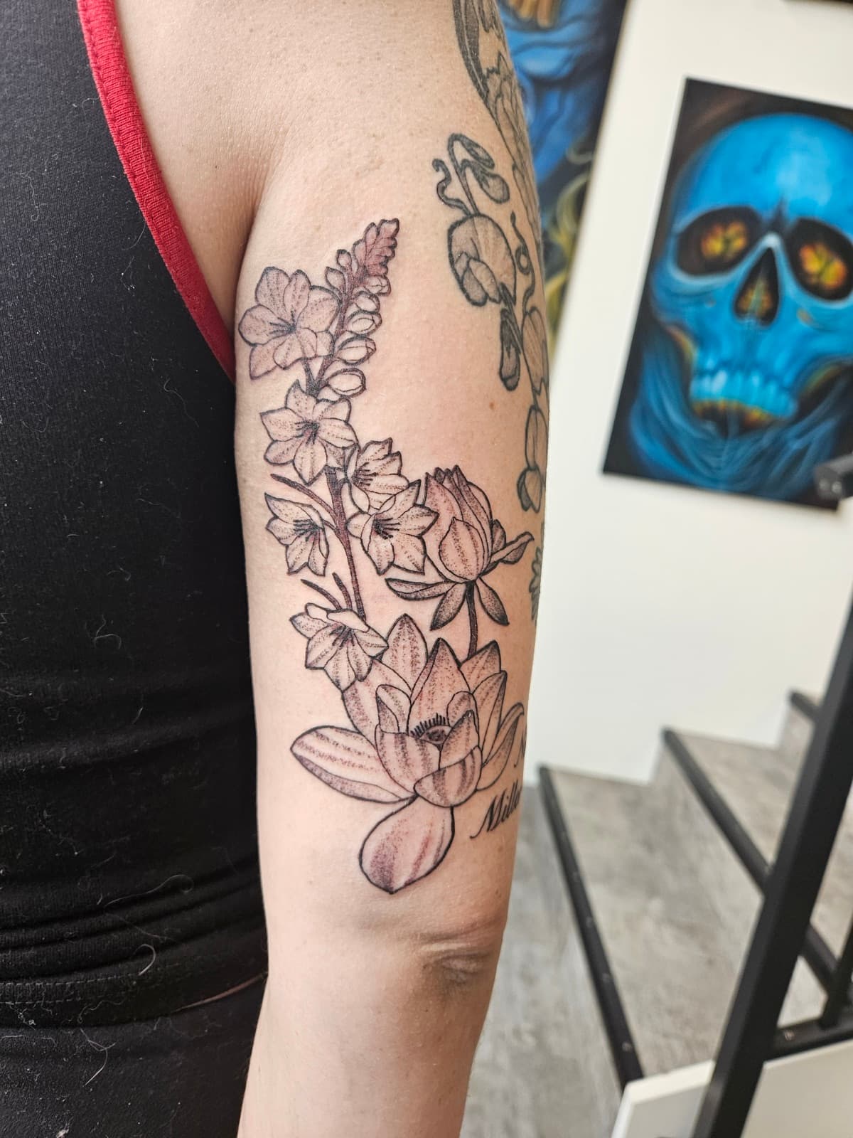 Lotus and larkspur flowers climbing the back of the arm, black linework