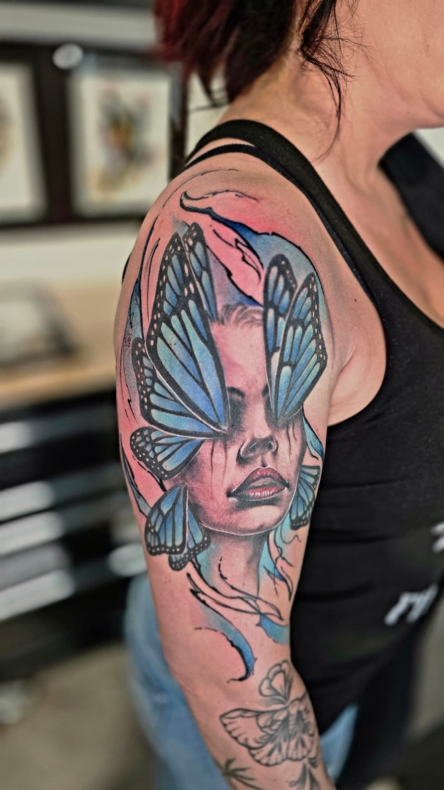 Woman’s face with blue butterfly wings over her eyes and blue watercolour splashes, colour on the upper arm