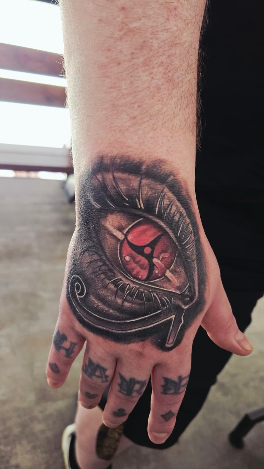 Realistic eye with a red patterned iris on the back of the hand, black and grey with red