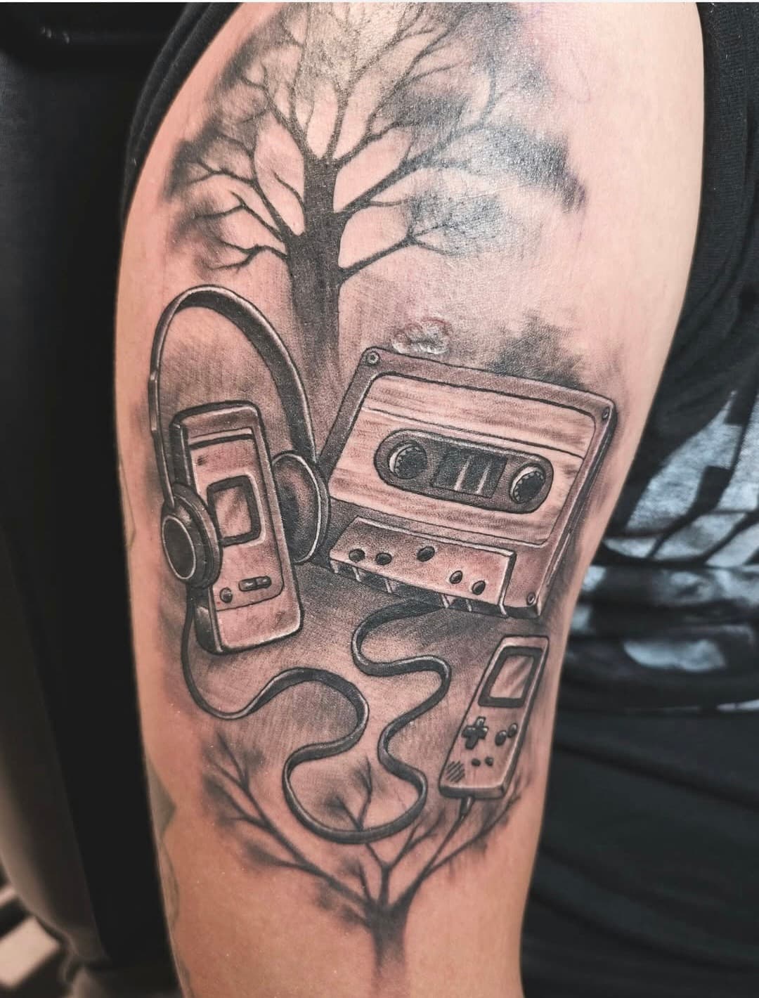 Cassette tape, a Walkman with headphones and a Game Boy under a bare tree, black and grey on the upper arm